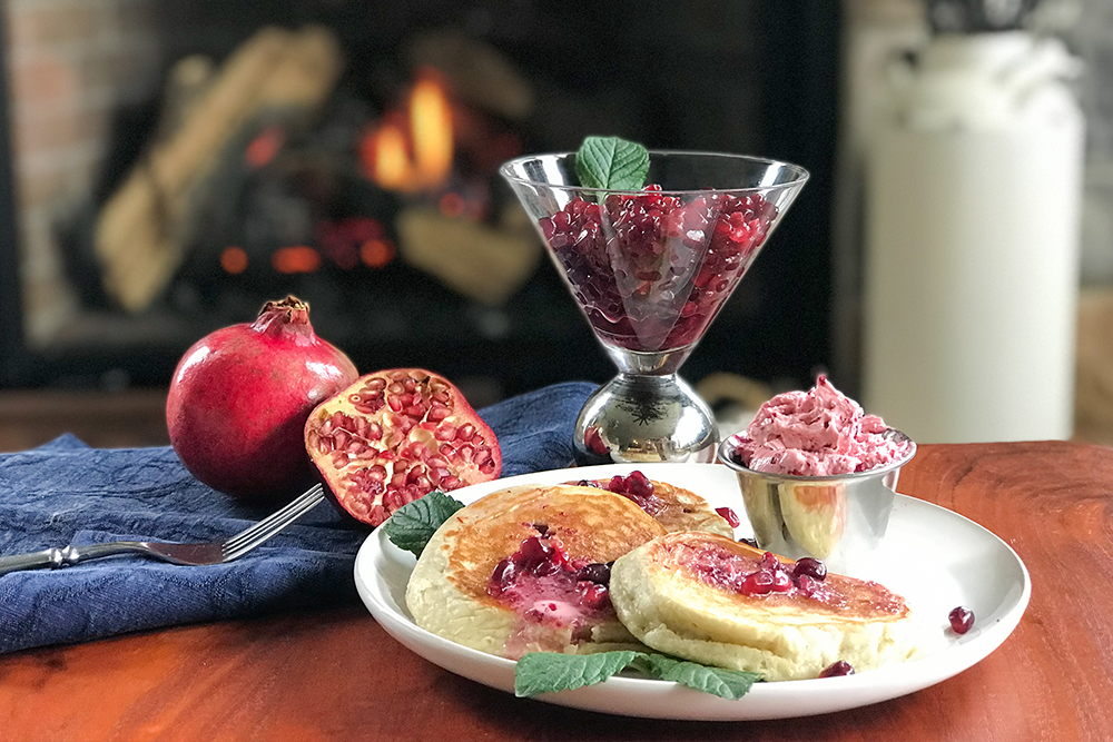 Photo of Pomegranate Pancakes served on a plate with whipped butter and pomegranate arils.