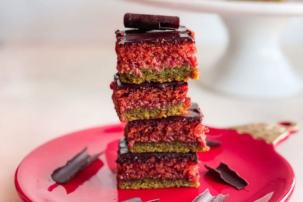 Paleo Rainbow Cookies stacked high on a red plate with chocolate shavings
