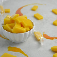 Mango flavored fruit chews in a bowl with a swirl of mango paste to the side and a wrapped peice of candy 