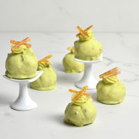 mini cream puffs covered in pistachio flavored white chocolate and topped with candied orange peel slices