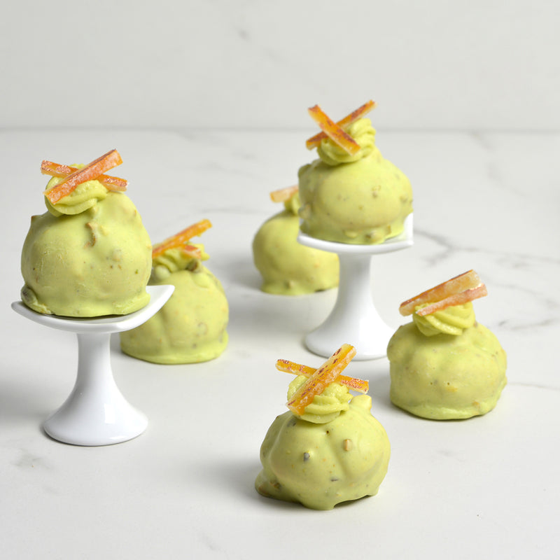 mini cream puffs covered in pistachio flavored white chocolate and topped with candied orange peel slices